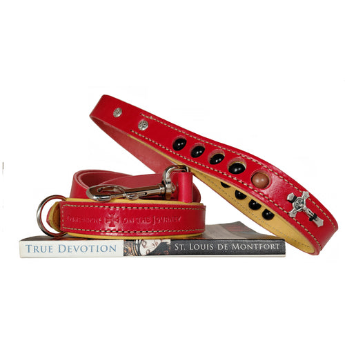 Red leather dog leash with deer skin tanned liner with rosary beads in handle and crucifix, sitting ontop of book True Devotion by St. Louis de Montfort